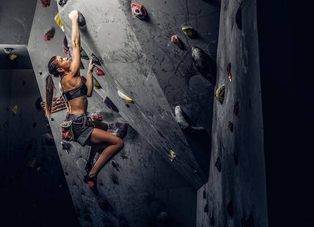 A young woman wearing sportswear practicing rock-climbing on a wall indoors