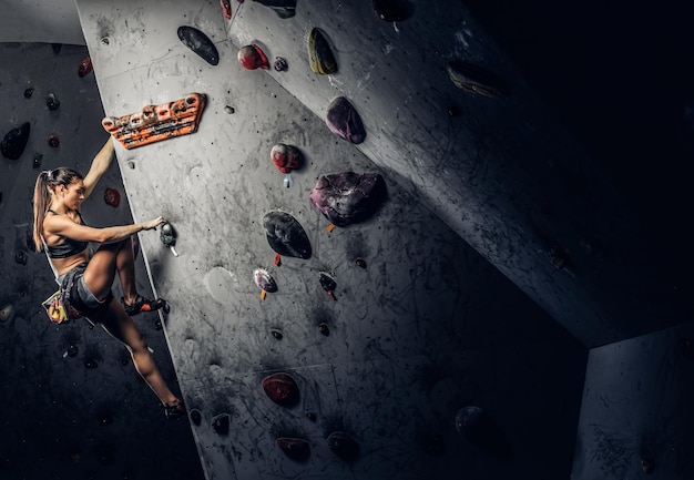 A young woman wearing sportswear practicing rock-climbing on a wall indoors