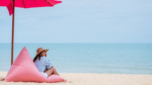 タイのビーチでスタイリッシュな青いドレスと青い空と麦わら帽子を身に着けている若い女性。