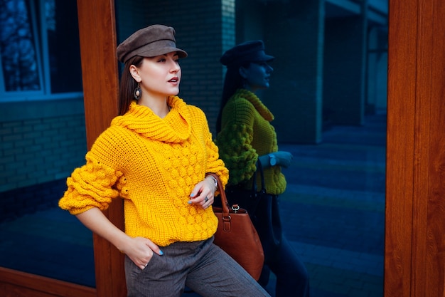 Young woman wearing stylish yellow jumper and holding handbag outdoors. Spring female clothes and accessories. Street fashion. Color of 2021