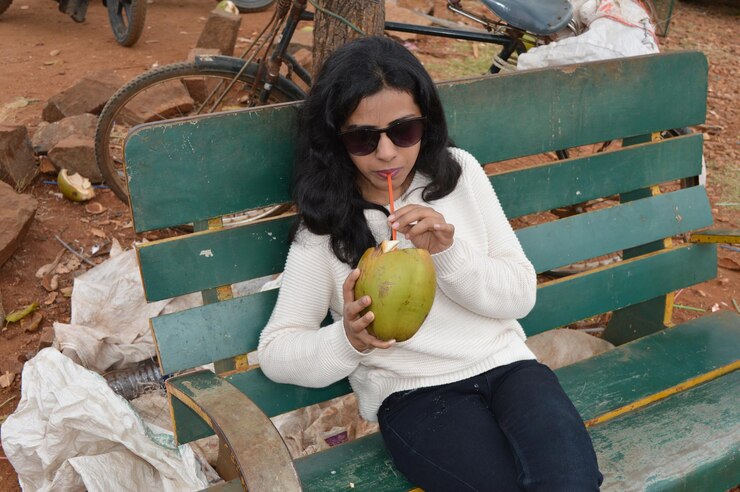 फोटो young woman wearing sunglasses drinking coconut milk while sitting outdoors