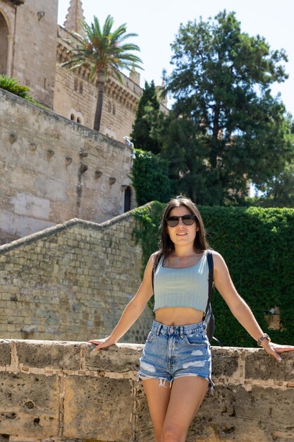 Young woman wearing sunglasses leaning against the wall in the Cathedral of Palma de Mallorca on a sunny day in Spain