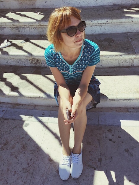 Молодая женщина в солнцезащитных очках сидит на улице