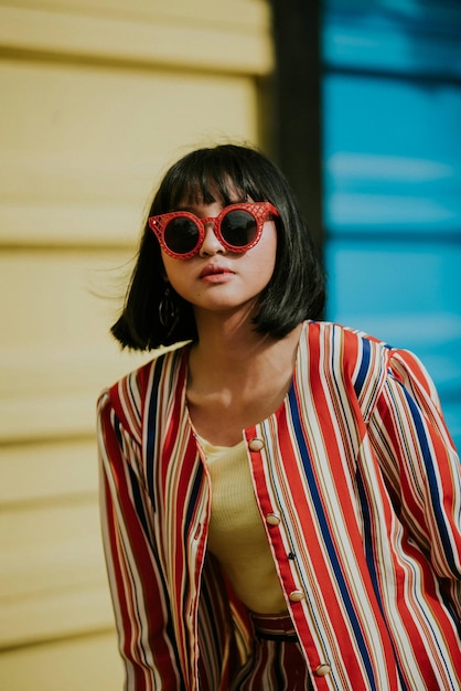 young woman wearing sunglasses standing against building in city