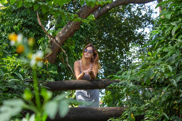 Young woman wearing sunglasses while leaning on tree railing in forest