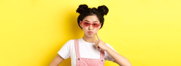 Young woman wearing sunglasses while standing against yellow background