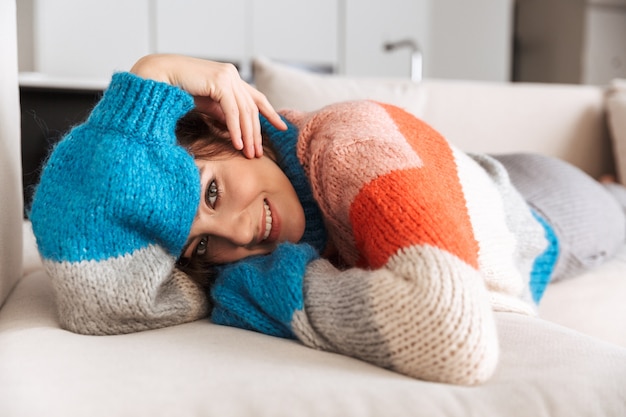 Foto giovane donna che indossa un maglione posa su un divano a casa