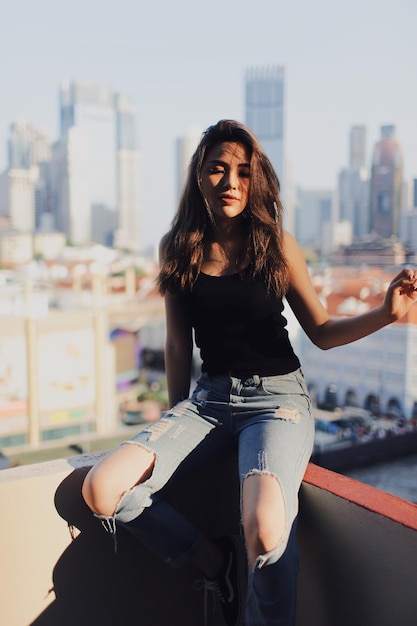 Молодая женщина в разорванных джинсах стоит против здания на террасе