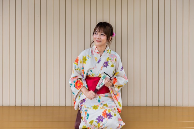 Young woman wearing traditional kimono sitting in Japanese style house with tea set with garden back