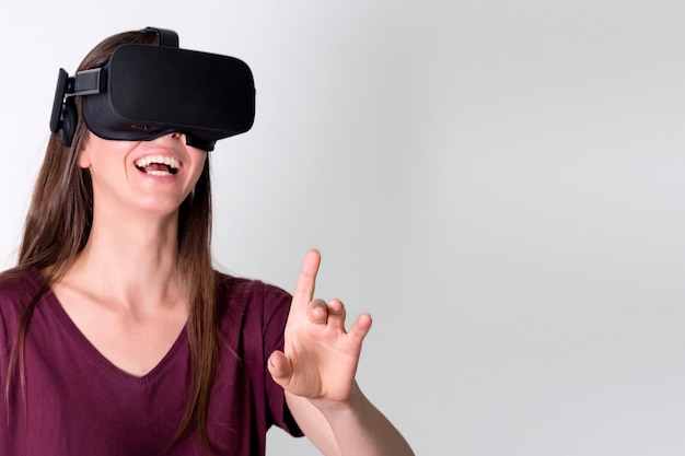 Cuffia avricolare d'uso degli occhiali di protezione di realtà virtuale della giovane donna, scatola del vr. connessione, tecnologia, nuova generazione, concetto di progresso. ragazza che prova a toccare gli oggetti nella realtà virtuale. studio girato su grigio