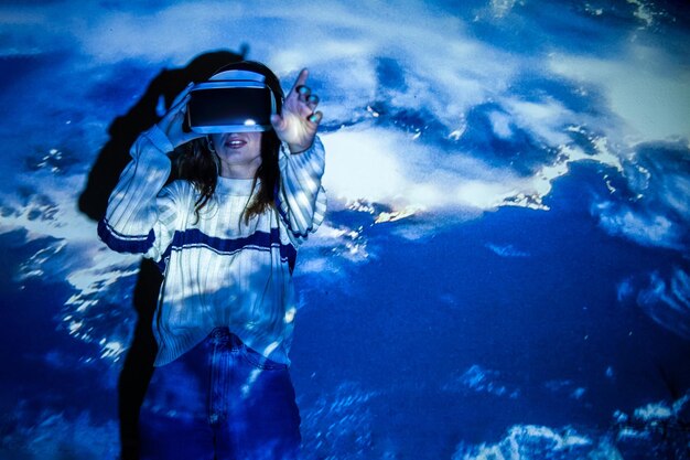 Photo young woman wearing virtual reality simulator standing against blue background