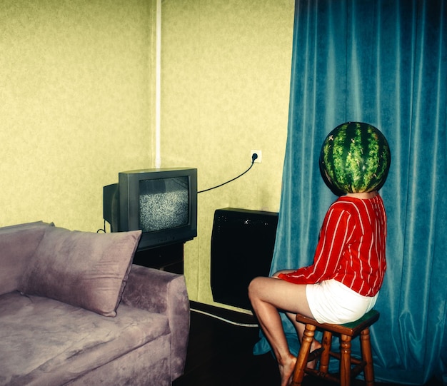 Photo young woman wearing watermelon on head sitting at home