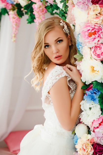 Young woman wearing wedding dress posing in room decorated with flowers