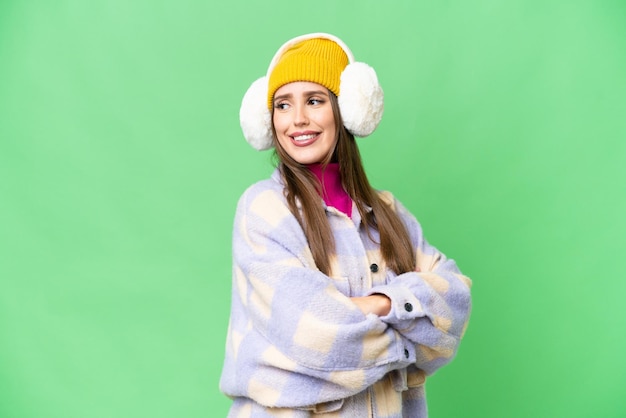 Молодая женщина в зимних муфтах на изолированном фоне хроматического ключа со скрещенными руками и счастливой