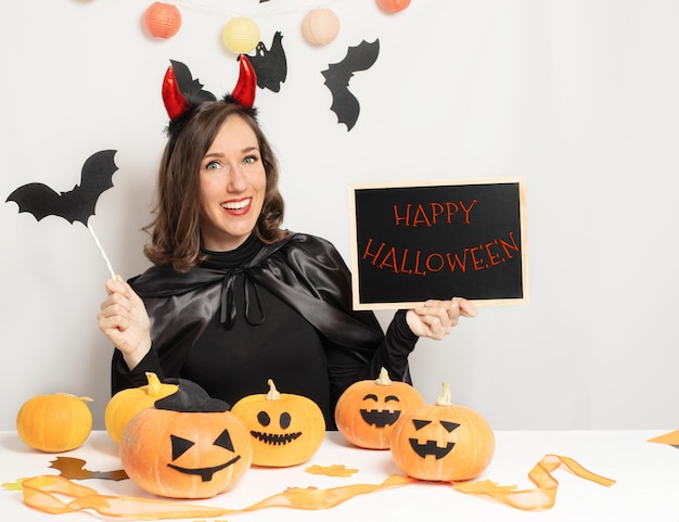 Giovane donna che indossa un costume da strega tiene una lavagna nera testo happy halloween sulla lavagna concetto di vacanza di halloween