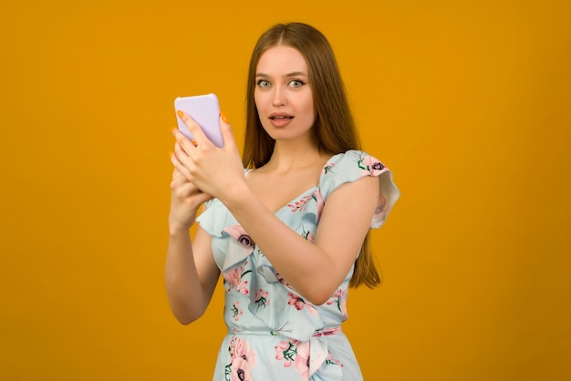 Young woman wears in sunner dress with flowers surprised by the news on a smartphone