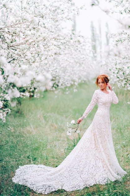 A young woman in a wedding dress is standing in a flowering spring garden