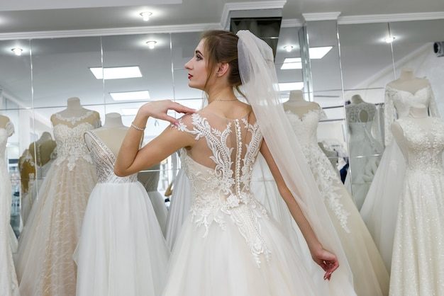 Giovane donna in abito da sposa e velo in negozio nuziale