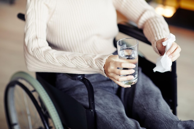 Young woman in wheelchair drinking water and wiping tears with napkin after emotional therapy sessio