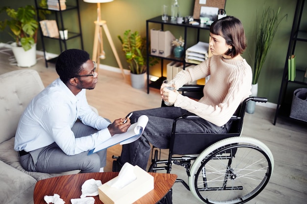 Young woman in wheelchair having private therapy session with psychologist to learn how to accept di