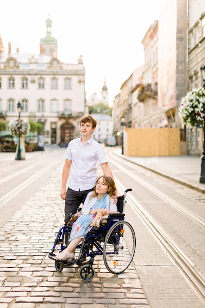 Молодая женщина в инвалидной коляске, прогуливаясь по городу вместе со своим молодым красавцем