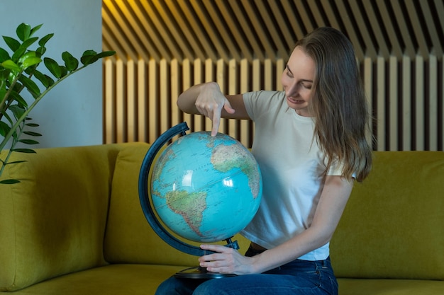 Foto giovane donna mentre è seduto sul divano a casa con in mano un globo del mondo sceglie un itinerario di viaggio