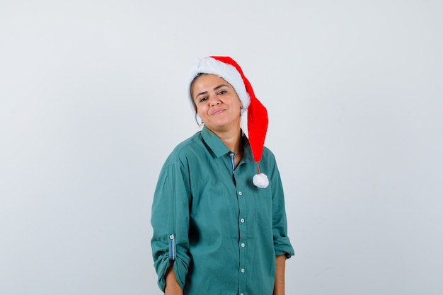 Young woman while standing in shirt, Santa hat and looking confident , front view.
