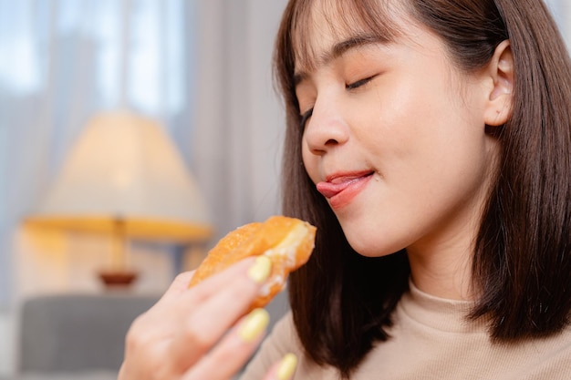 Giovane donna mentre guarda la tv, si rilassa, mangia spuntino e ciambella ordinando la consegna, a casa in vacanza. cibo spazzatura, pasto malsano, rischio di obesità.