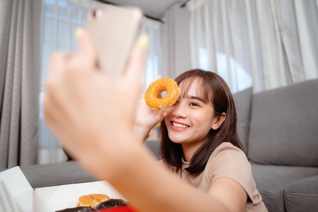 젊은 여성은 휴일에 집에서 배달을 주문하여 TV를 보고, 휴식을 취하고, 간식과 도넛을 먹습니다. 정크 푸드, 건강에 해로운 식사, 비만 위험.