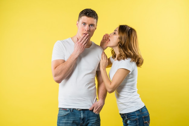 Young woman whispering something in shocked boyfriend's ear