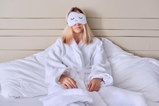 Young woman in white bed in bathrobe eye mask Healthy lifestyle sleep rest beauty concept