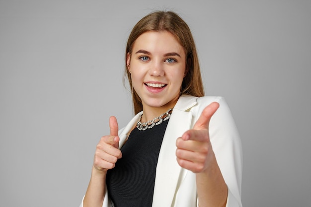 Photo young woman in white blazer pointing at you against a grey background