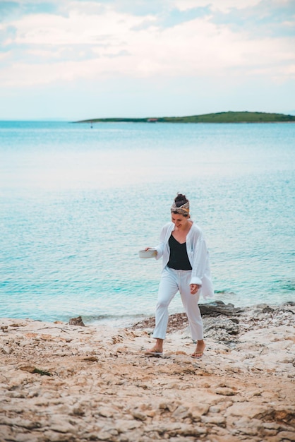 Young woman in white clothing walking by rocky sea beach