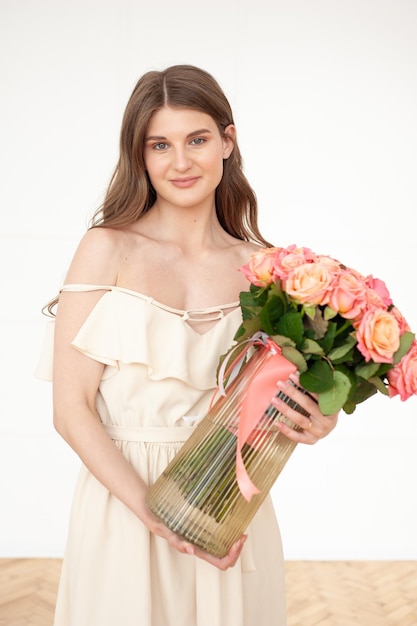 A young woman in a white dress holds a bouquet of roses.