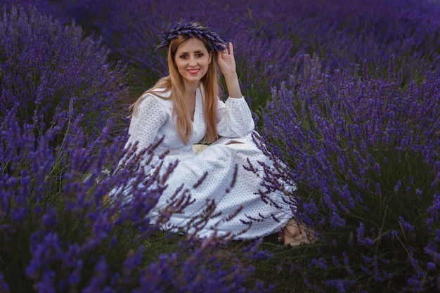 A young woman in a white dress sits in the middle of a lavender field