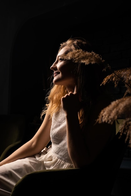 Una giovane donna in abito bianco siede pensierosa su una poltrona in una stanza buia concetto di introspezione di solitudine
