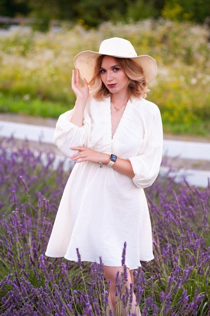 Young woman in a white dress and straw hat running in a lavender field