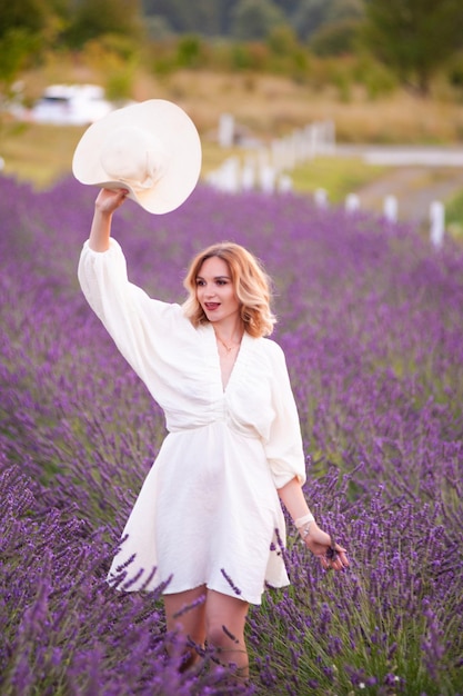 Young woman in a white dress and straw hat running in a lavender field