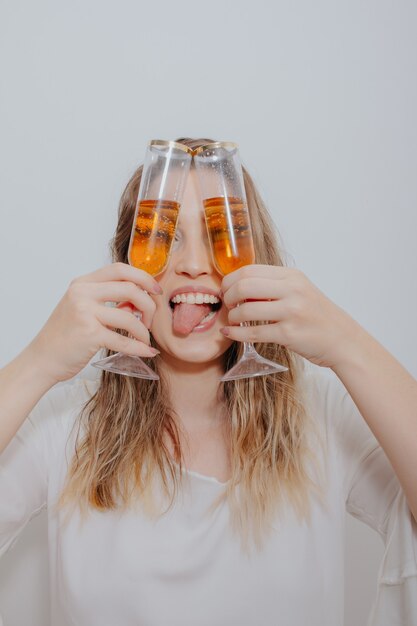 Young woman in white dress and with two glasses of sparkling wine in hands in front of her face