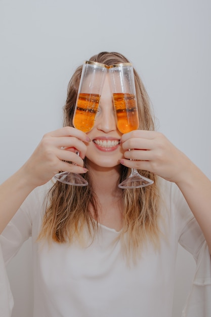 Young woman in white dress and with two glasses of sparkling wine in hands in front of her face