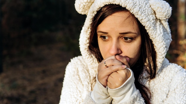 A young woman in a white fluffy hoodie shrinks from the cold in the forest