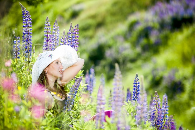 Young woman in white hat with basket of lupine resting on the nature