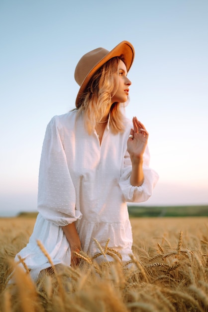 Young woman in white linen dress and hat enjoying a sunny day in a golden wheat field Summer beauty