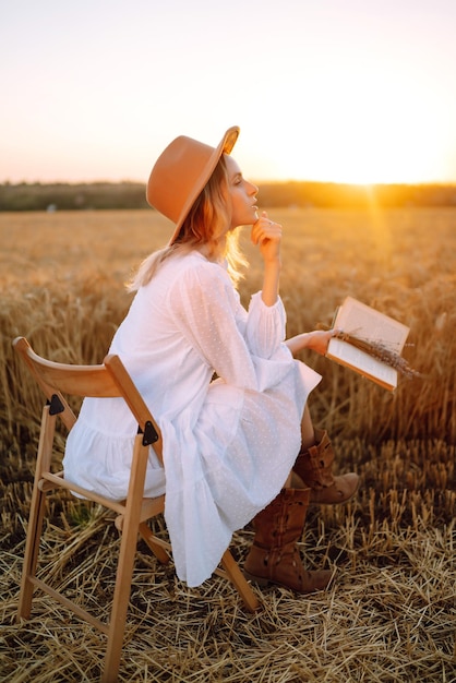 Young woman in white linen dress and hat enjoying a sunny day in a golden wheat field Summer beauty