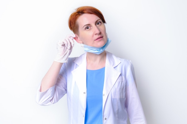 Young woman in white medical gown takes off her medical mask.\
portrait of female doctor