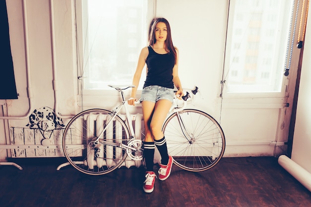 Young woman on white retro bicycle, posing in the apartment indoor