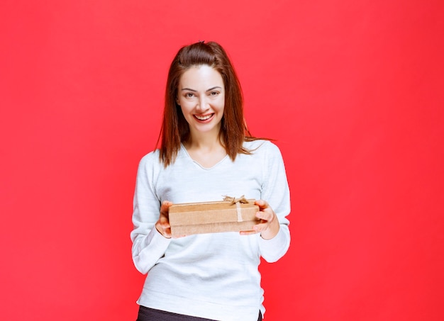 Young woman in white shirt holding a cardboard gift box and giving it to her friend