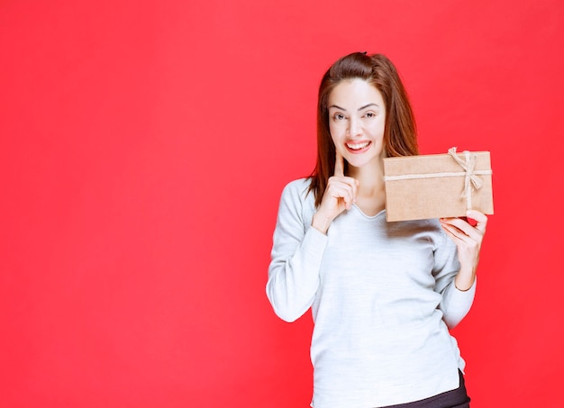 Young woman in white shirt holding a cardboard gift box and looks confused and thoughtful