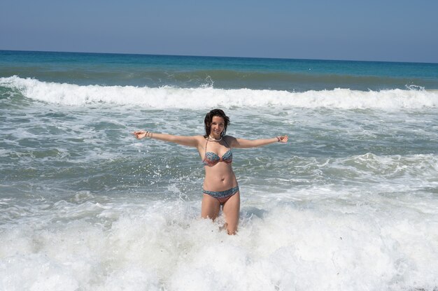 Young woman in a white shirt is bathes in the waves in the sea foam on an exotic tropical island. High quality photo