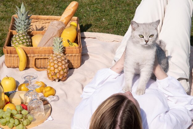 A young woman in a white shirt is resting on a picnic with her pet kitten